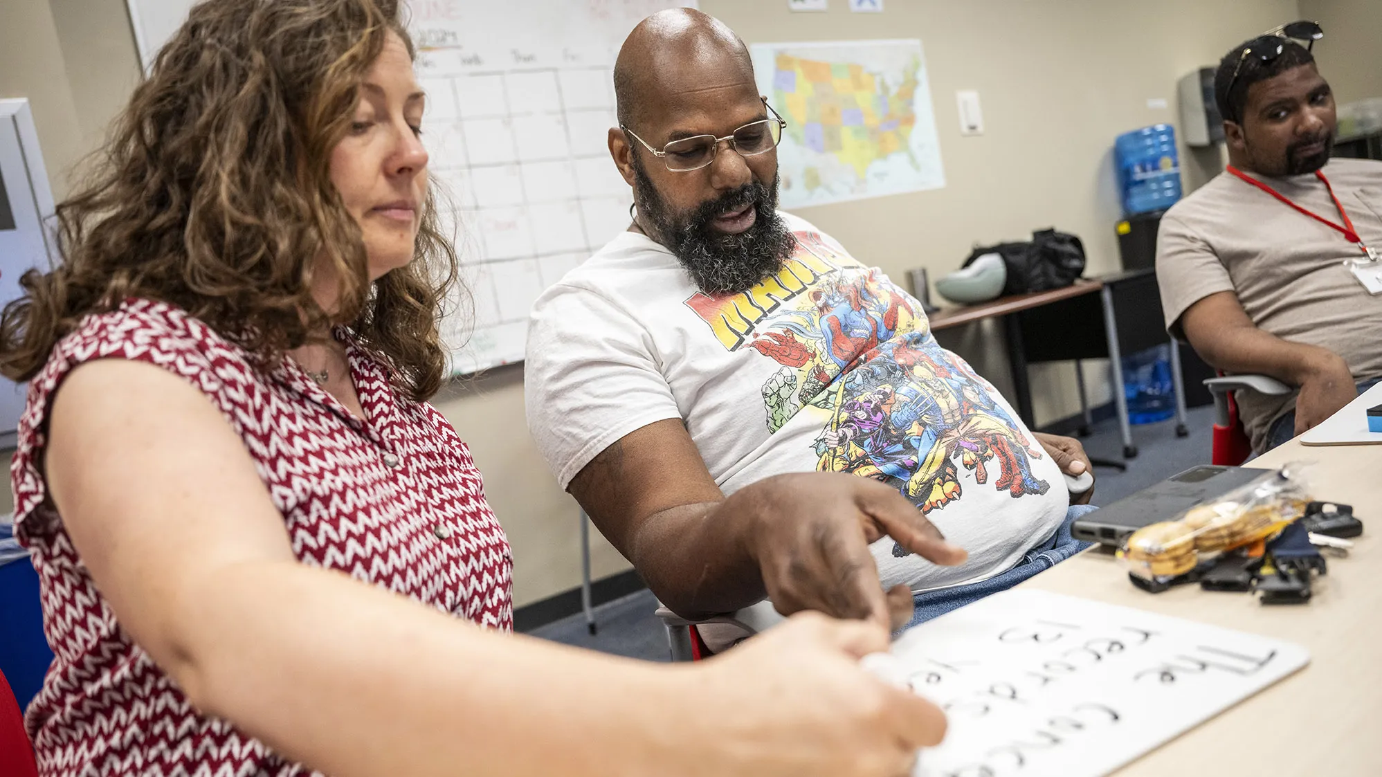 Ray Myers lounges in his chair at a worktable, pointing at big words and smiling as he reads them. His speech therapist, Arin Sheeler, also points at the words as she sits up straight in the chair next to him.