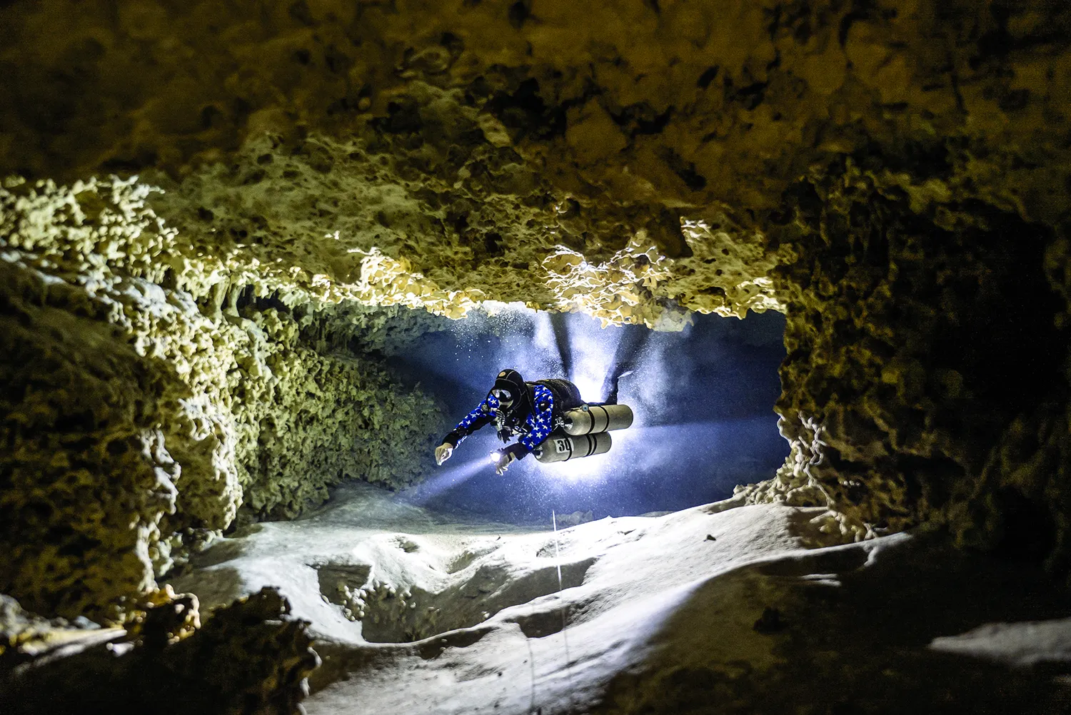 Matt Scantland, in scuba gear with two oxygen tanks, swims through an underwater cave