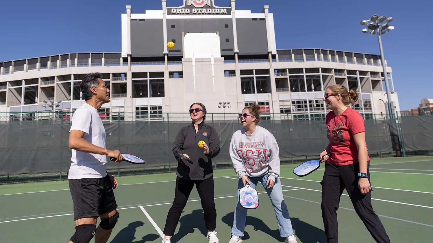 On a practice field near Ohio Stadium, four co-workers have a blast playing pickleball.