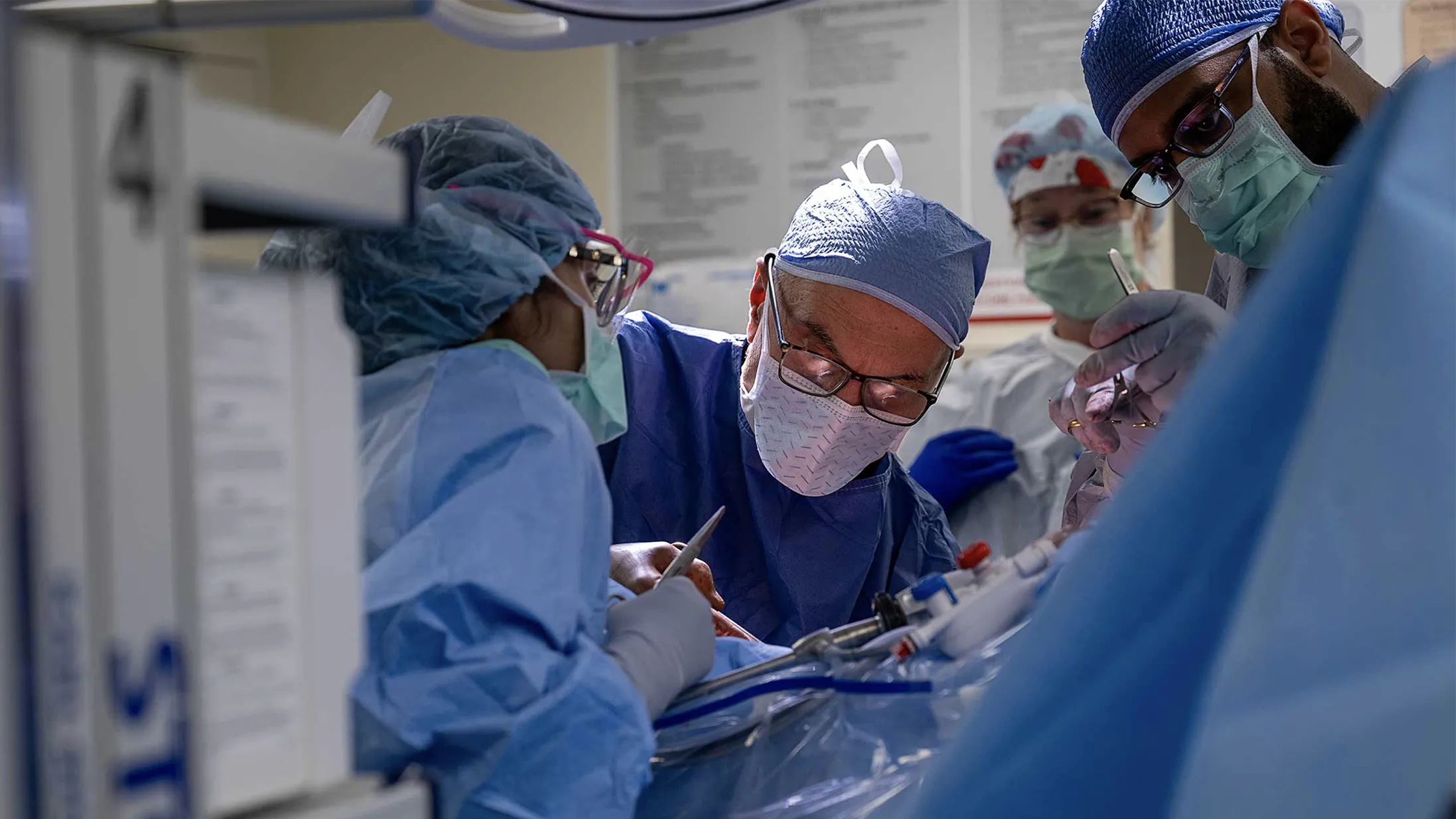 A team of Ohio State Wexner Medical Center employees works in the operating room to remove a donor's kidney. Ther are all suited up in scrubs, face masks and caps and lean over the patient, who cannot be seen.