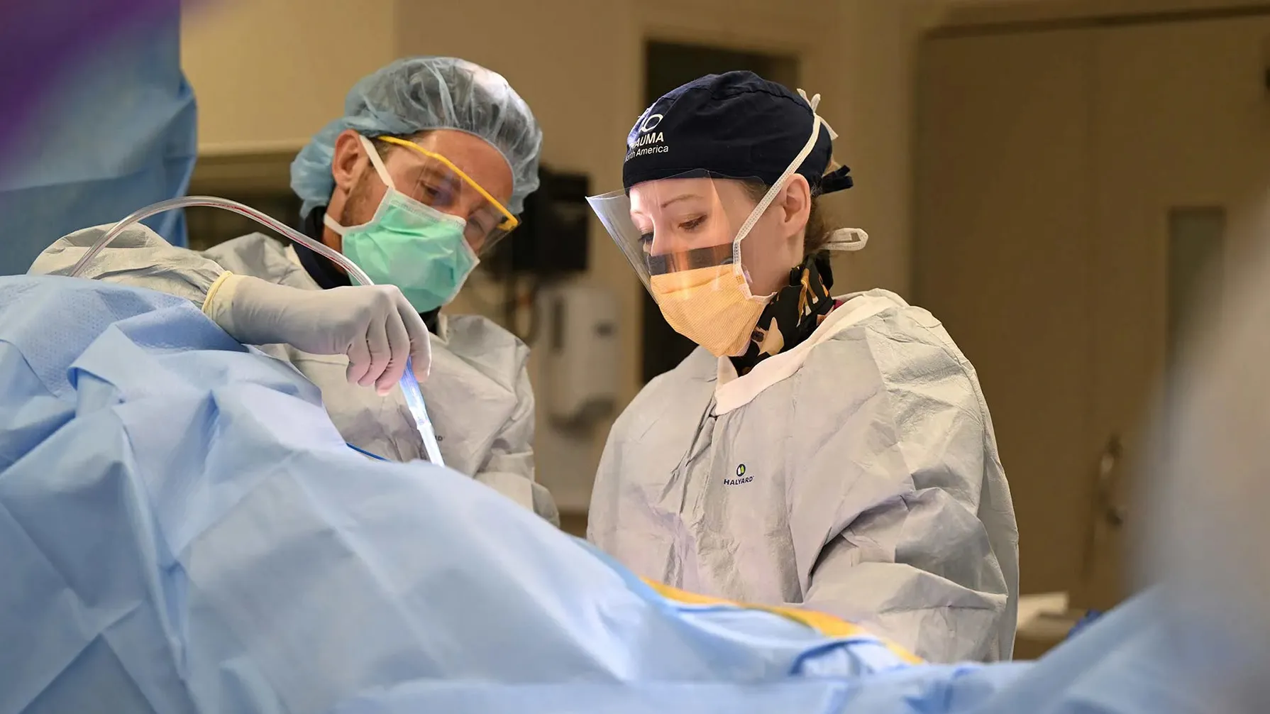 Orthopedic surgeon Angela Collins is covered in protective gear during a surgery in a hospital operating room. A man, similarly gowned-up, assists.