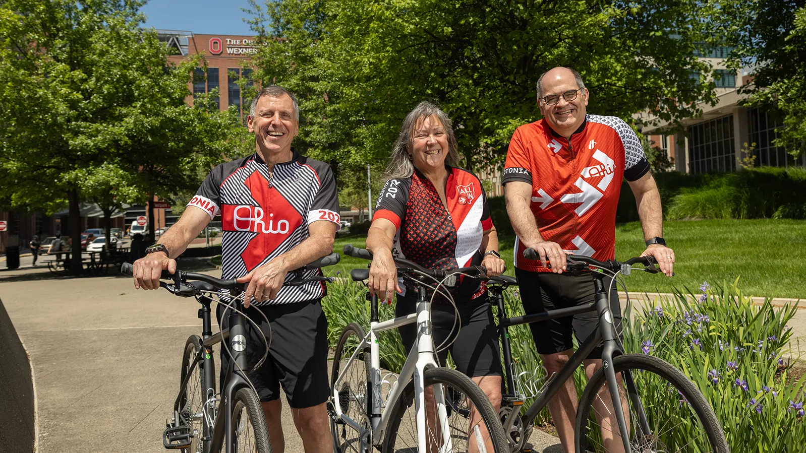 Three people in Ohio State bicycle jerseys pose for a photo with their bicycles. They're laughing and seem to be having a good time.