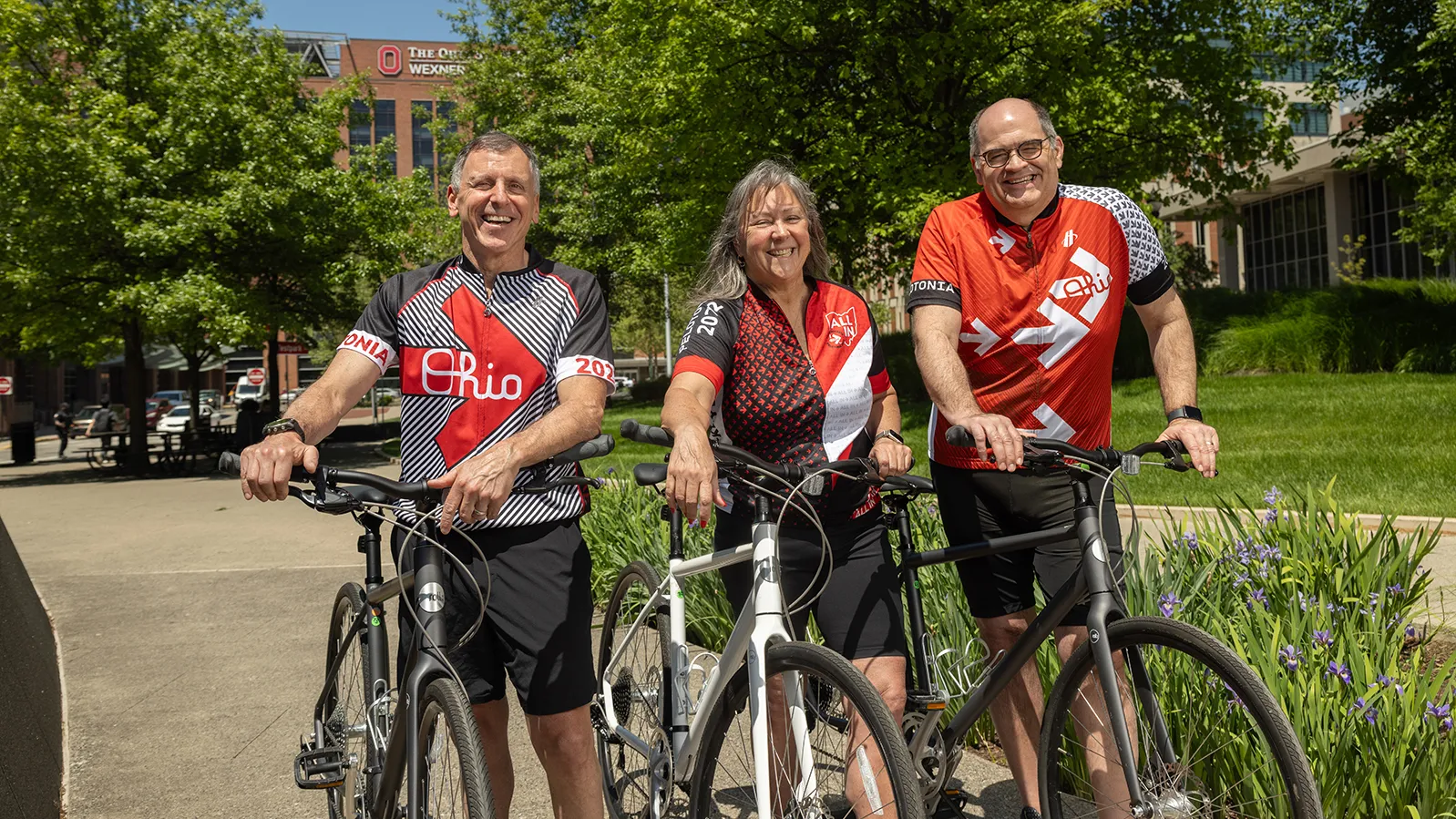 Three people in Ohio State bicycle jerseys pose for a photo with their bicycles. They're laughing and seem to be having a good time.