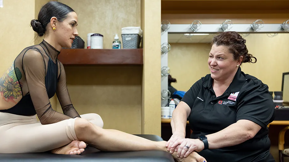 An athletic trainer touches a dancer's foot while watching for how she responds.