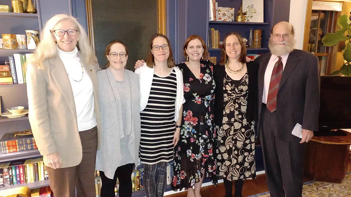 An informal family photo shows the parents and their four children, who are now grown into adults, posing with arms around each other and dressed up.
