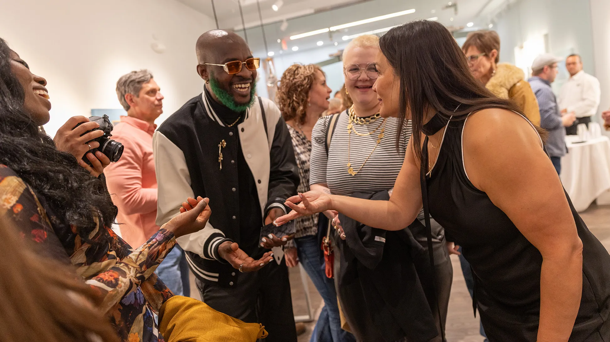 Michelle Brands greets visitors to her newly opened gallery, including a Black man with green beard, whom she is making eye contact with as she leans toward him.