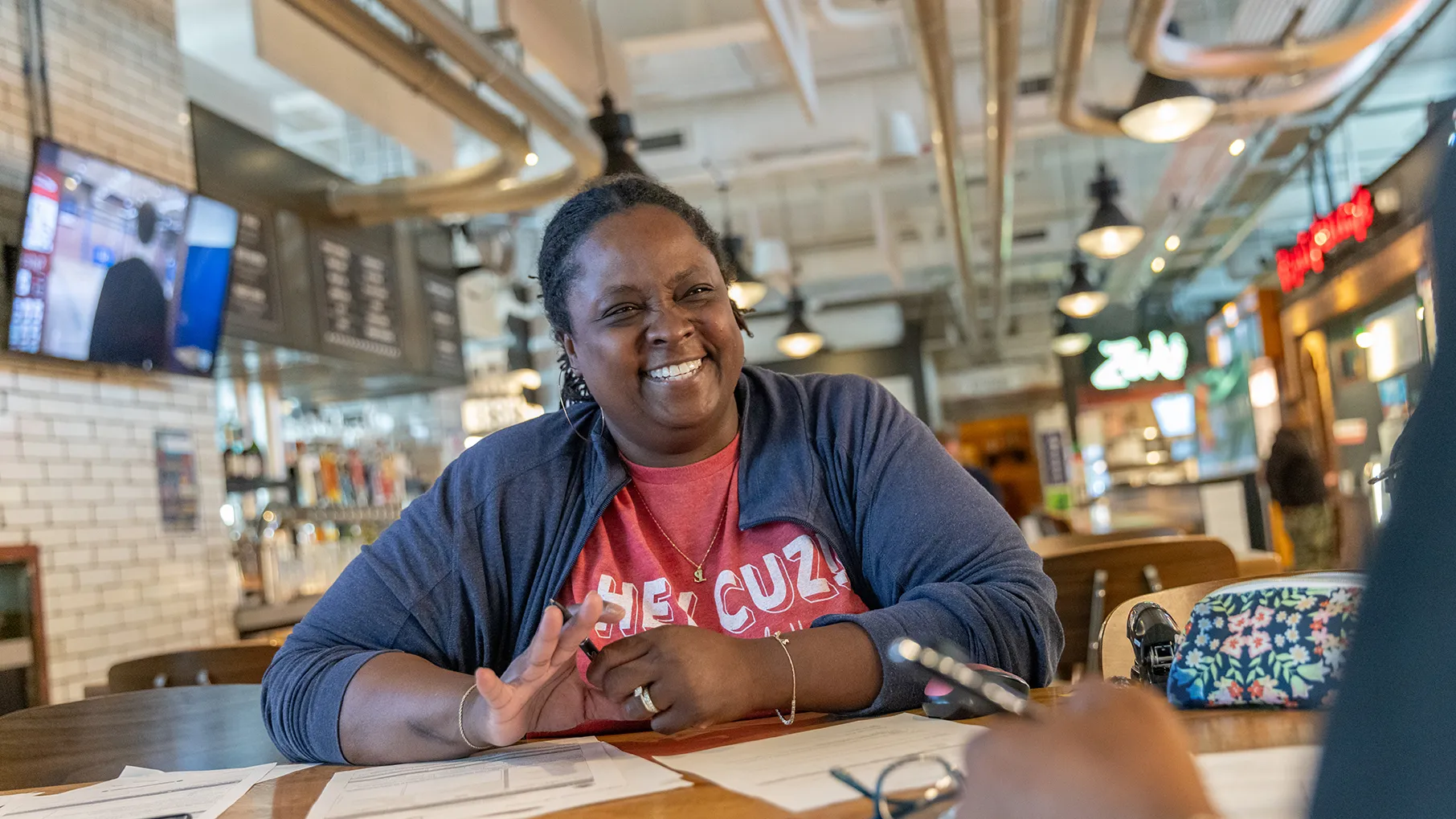 Sadaya "Daisy" Lewis sits at a hightop table to onboard an employee. This food hall is where her popular Modern Southern Table restaurant is located. There is exposed, shiny ductwork, white brick walls and a clean, modern feel.