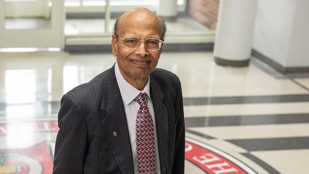 Milap Nahata, an Indian man, poses for a portrait in the lobby of the pharmacy college at Ohio State. Its colorful insignia is painted on the floor, adding an interesting background. Nahata looks calm, confident and friendly.