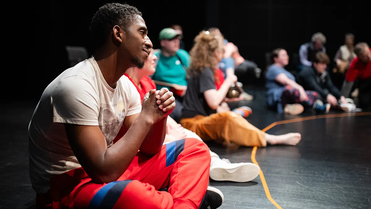 Sitting on the floor of an auditorium in a big circle are a young Black man and others with autism, as well as ohio state students. They're getting ready to participate in a special Shakespeare and Autism program