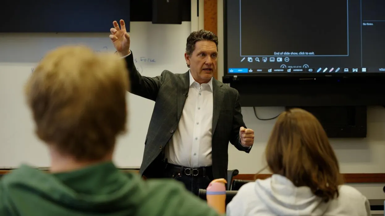 Ohio State alumnus Jeff Prestel talks to students during a class at Fisher College of Business. He stands in front of them, arm raised as he gestures to make a point. He seems professional and focused.