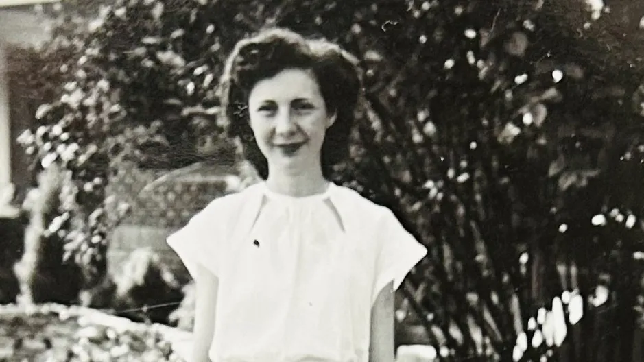 As a young woman in this black and white photo, Ruth Klingler McPheron stands in front of a house and greenery wearing a white blouse and shin-length plaid skirt. She is a white woman with a pretty hairstyle, a soft smile and the looks of someone you'd want to tell stories to.
