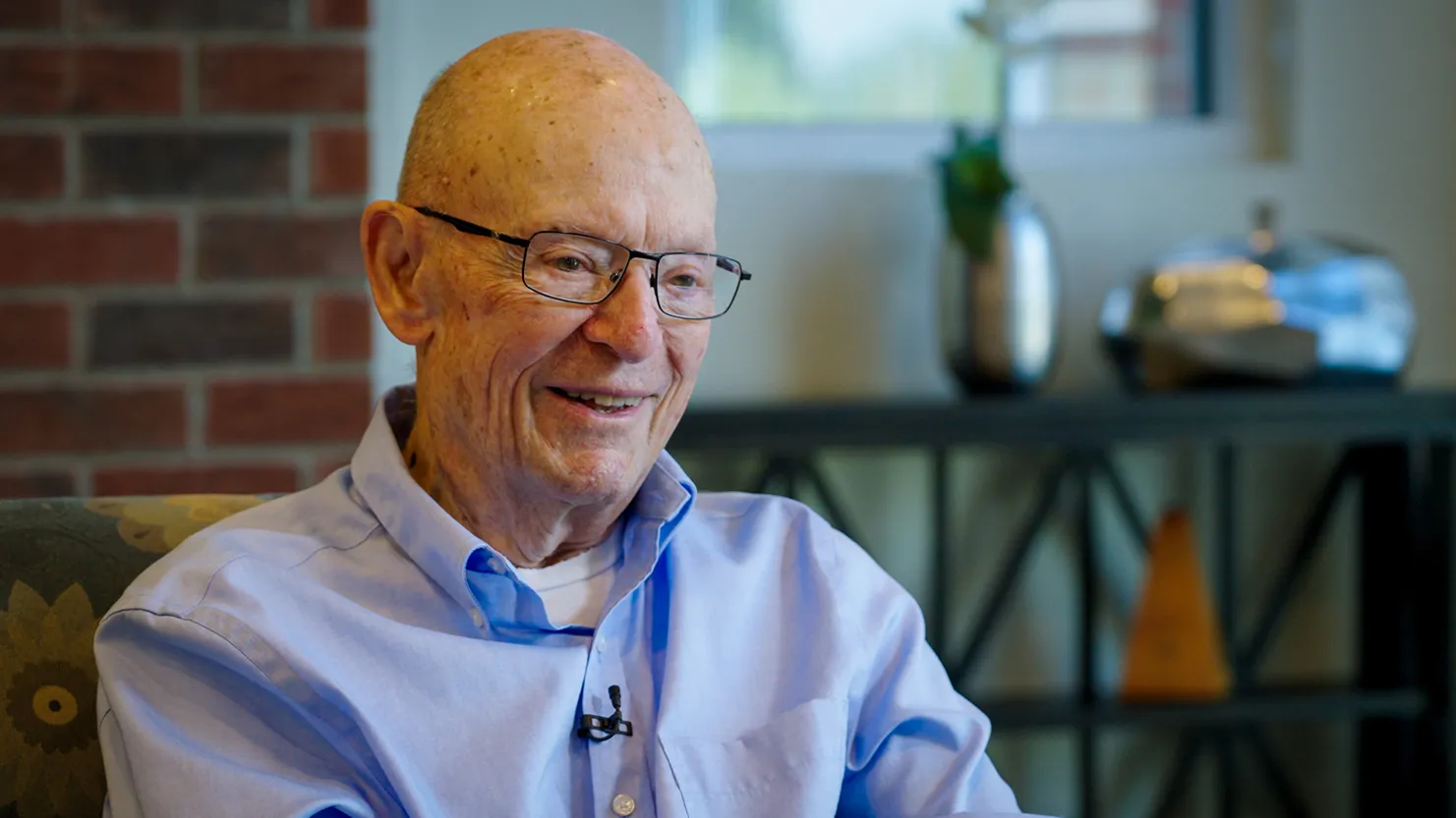 Dick Wood smiles as he tells a story. He's an older white man wearing glasses and a button-up shirt. Lines on his face shows he's smiled a lot through his years.