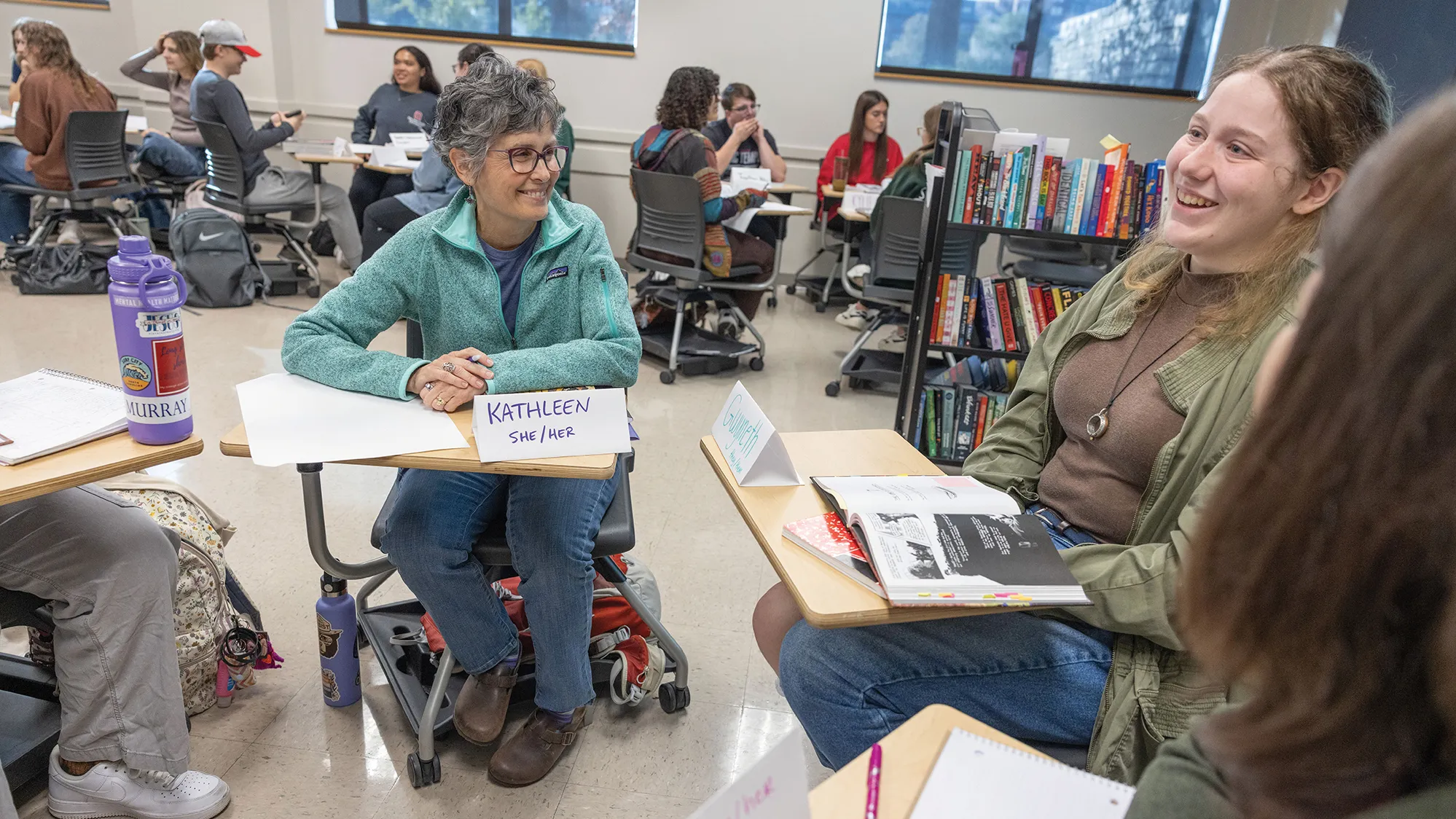 An older woman with short gray hair smiles as she watches a young woman of traditional college student age talk during a small group discussion inside an Ohio State classroom.