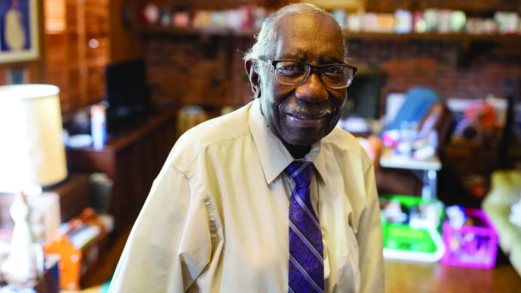 Osiefield Anderson is shown as an old black man with a friendly smile. He wears thick-rimmed glasses, a button down shirt and a brightly colored tie and seems to be in a home office.
