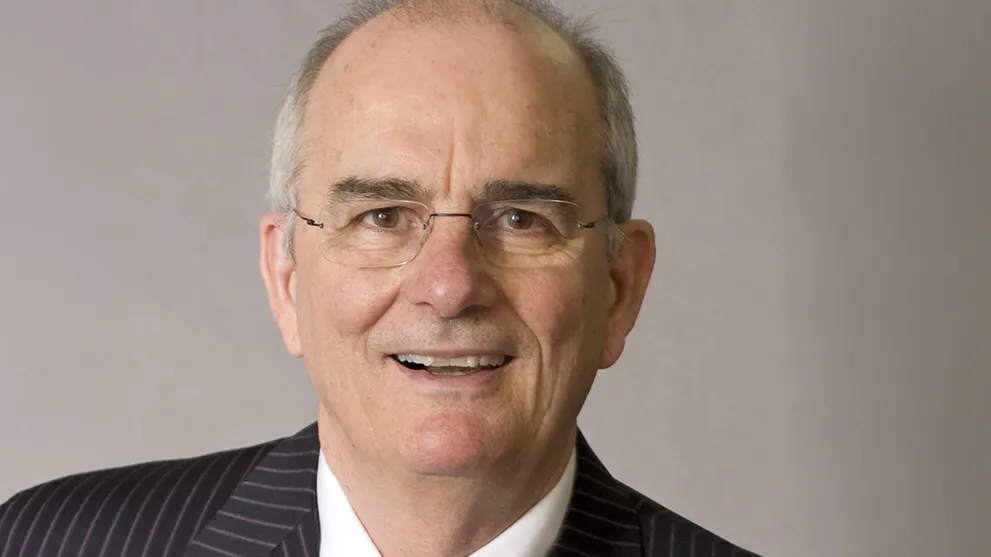 Gregory Williams wears glasses, a suit and an open mouthed smile. He looks like he's laughing as he poses for this formal portrait.