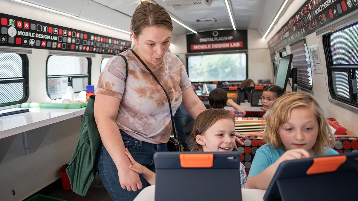 A mom oohs while her two children each sit in front of an iPad inside the STEM bus