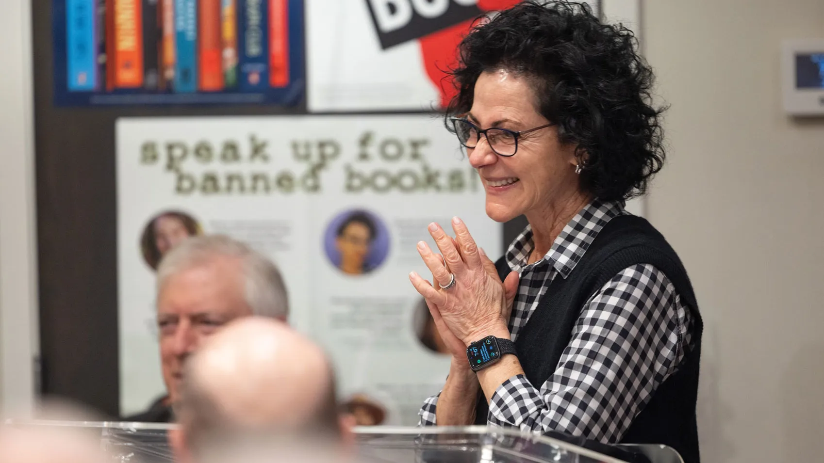 Linda Kass clasps her hands near her heart as she stands at a lectern in front of a crowd in her shop and introduces the visiting author and other guest performers. She's smiling genuinely--it's apparent she enjoys what she's doing.