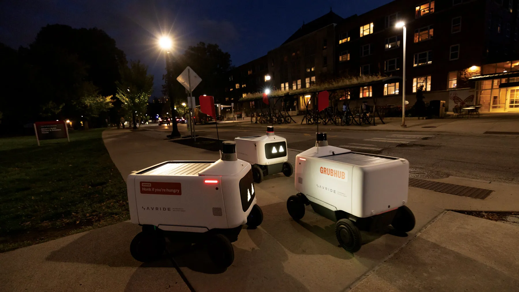 Three robots seem to meet. They face one another in the dark as lights shine around them.