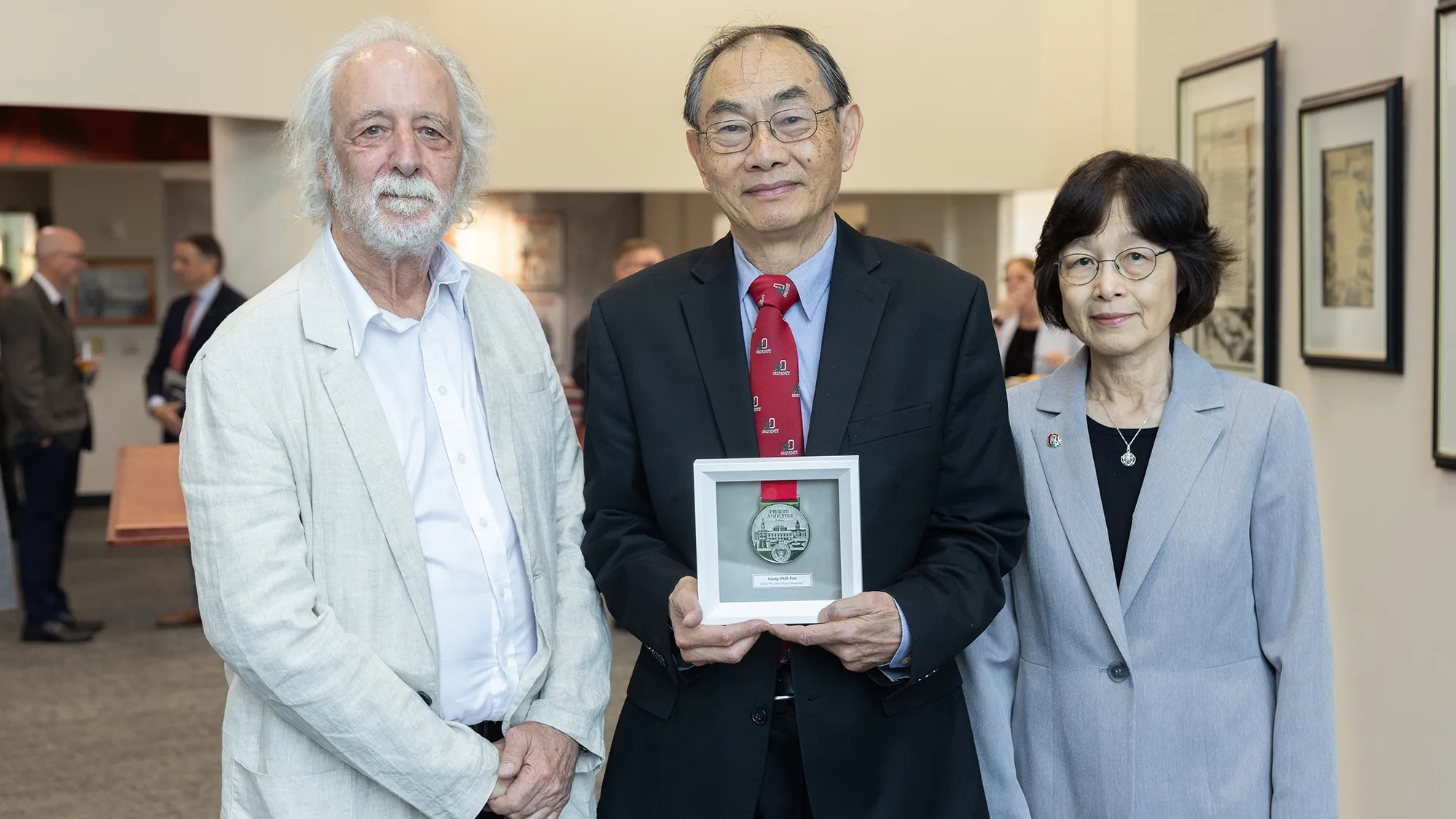 Dr. Liang-Shih Fan proudly holds his framed Agostini medal while flanked by Pierre Agostini and Fan's wife. The couple are Chinese; Agostini is a white man with beard and longish hair. They all have small, proud smiles.
