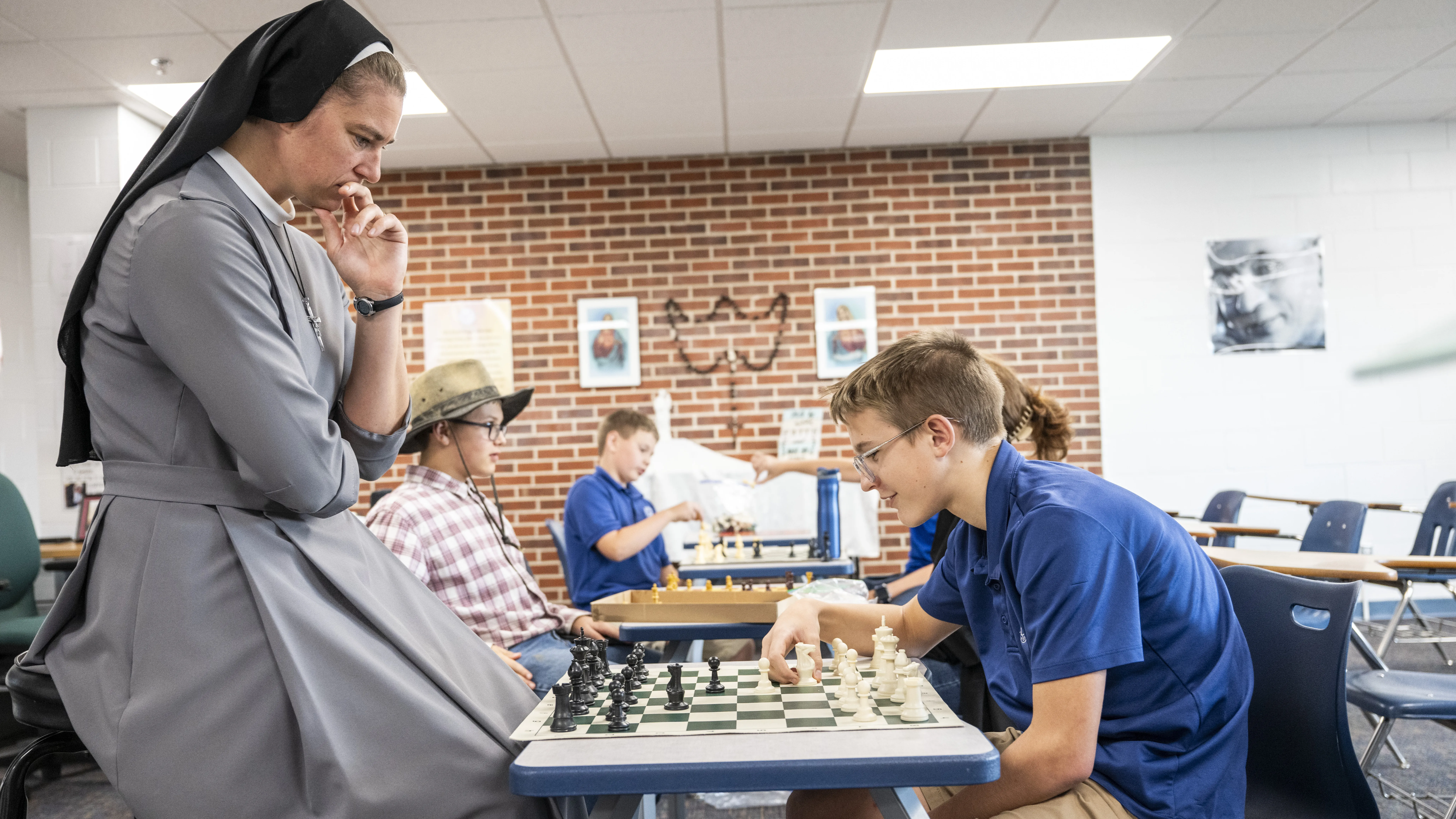 Sister contemplates her next move as she sits across a chess board from a middle school student.