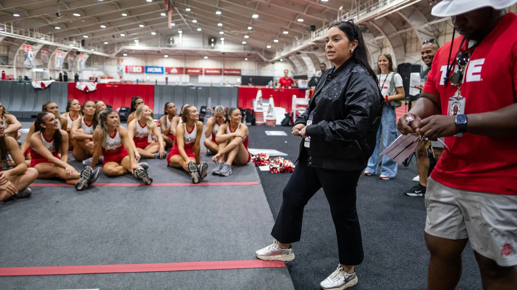Melissa stands in front of a meeting of the full spirit program as she talks about the day ahead. The students all sit on the floor looking up at her.