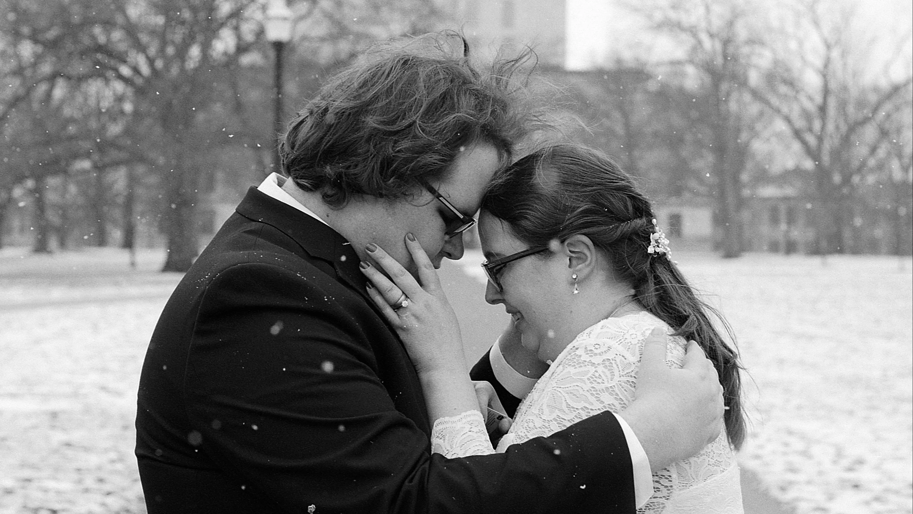 A bride and groom touch foreheads on The Oval as it snows in this black and white photo.