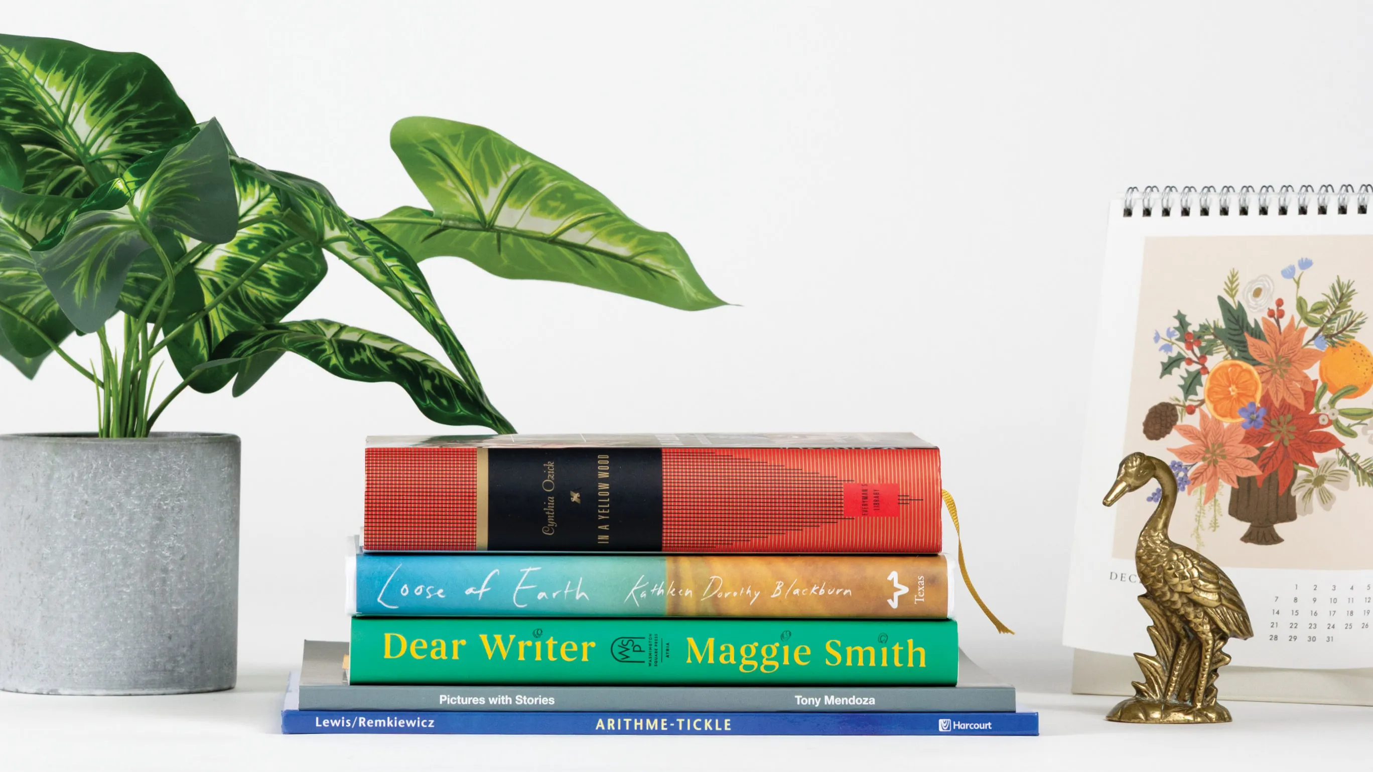 A photo shows the books in this story stacked on their side, alongside a plant, mini calendar with flowers and a small golden crane statue