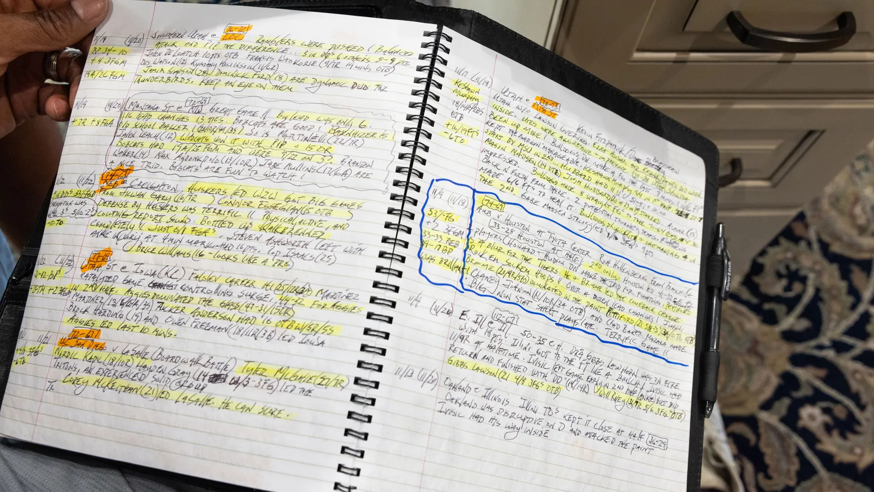 Kellogg holds open a spiral notebook filled with handwritten notes. The pages are densely covered with writing, highlighted sections, and marked passages, including one area outlined with a rectangular border. 