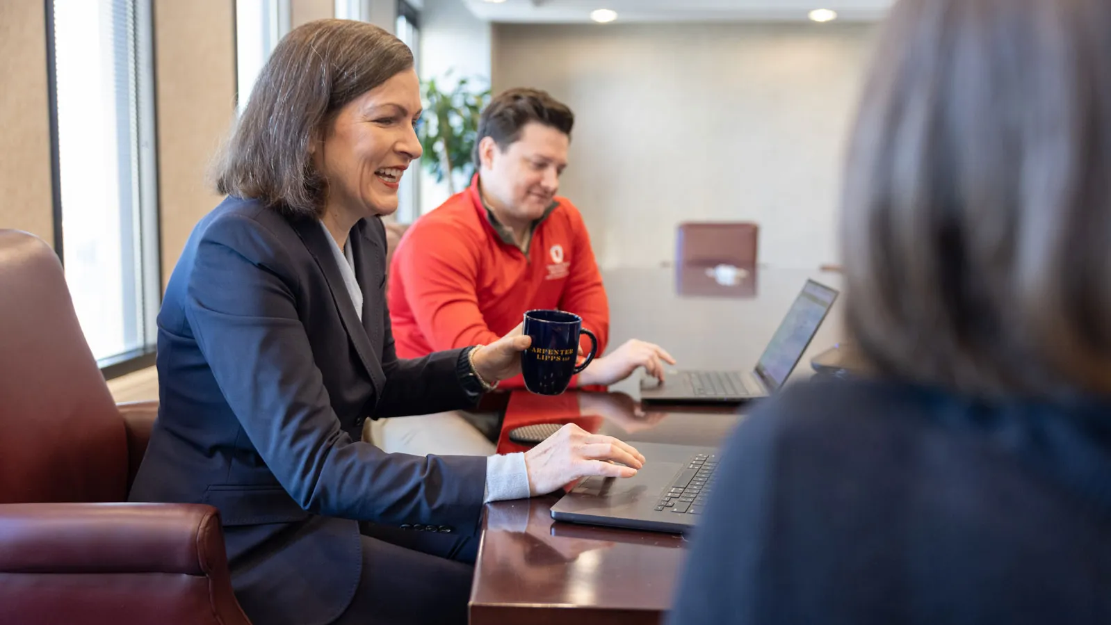 Lloyd and others laugh as they sit around a conference table using laptops.