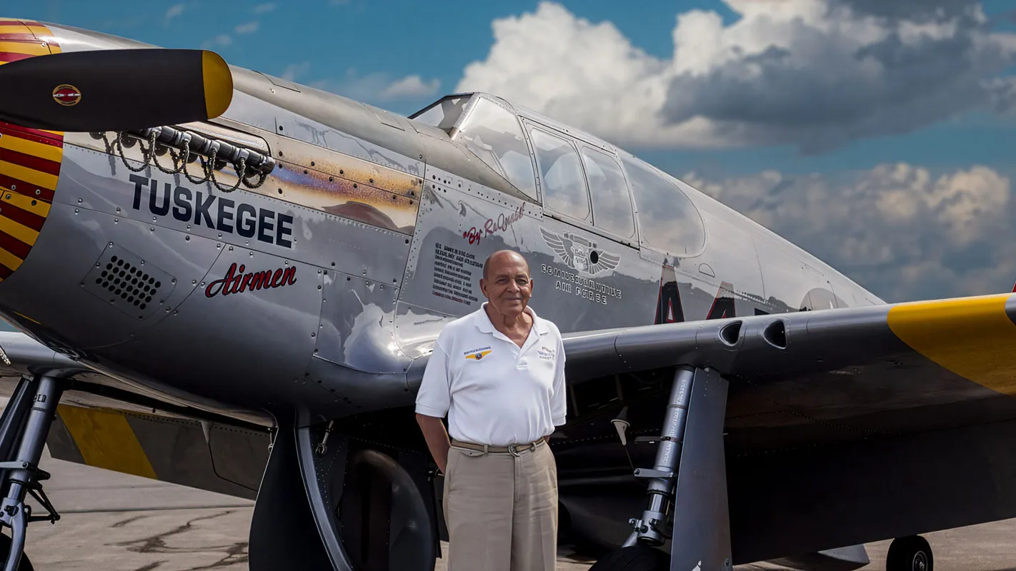 AN older black gentleman stands in front of an airplace with "Tuskegee Airmen" stenciled on the side. It's a plane like what he flew during World War II.