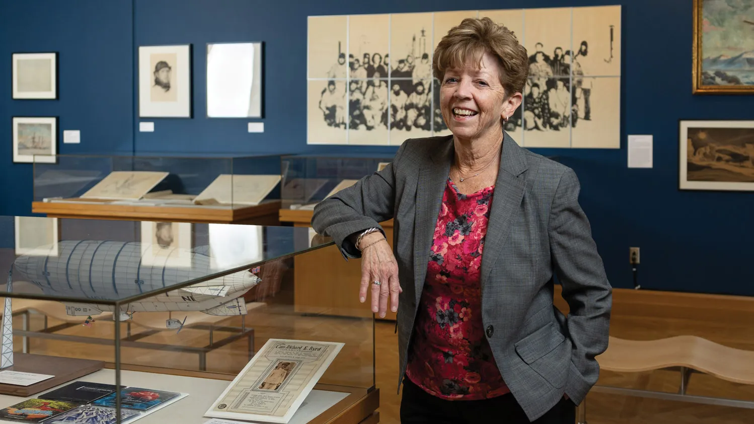 Laura Kissel stands in a museum exhibit she designed with polar artifacts. She’s laughing, wearing a suit coat and colorful shirt, and has an elbow propped on a glass display case. She looks like she’d be a fun co-worker.