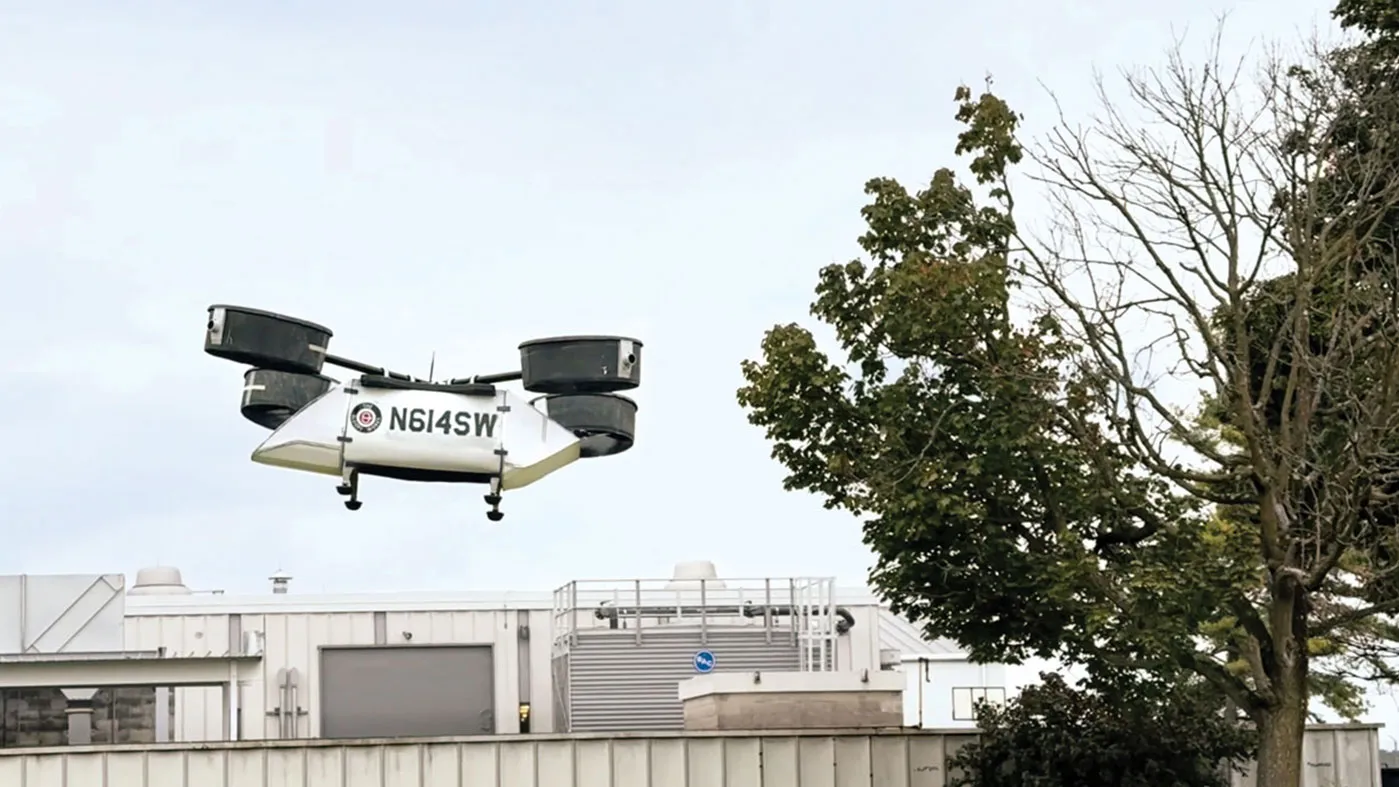 A model rescue drone created at Ohio State flies into the air. It has a large body to ferry people or supplies and 8 propellers enclosed in four cannisters, each at the end of a pole. Together, they're laid out as a helicopter's rotors would be.  
