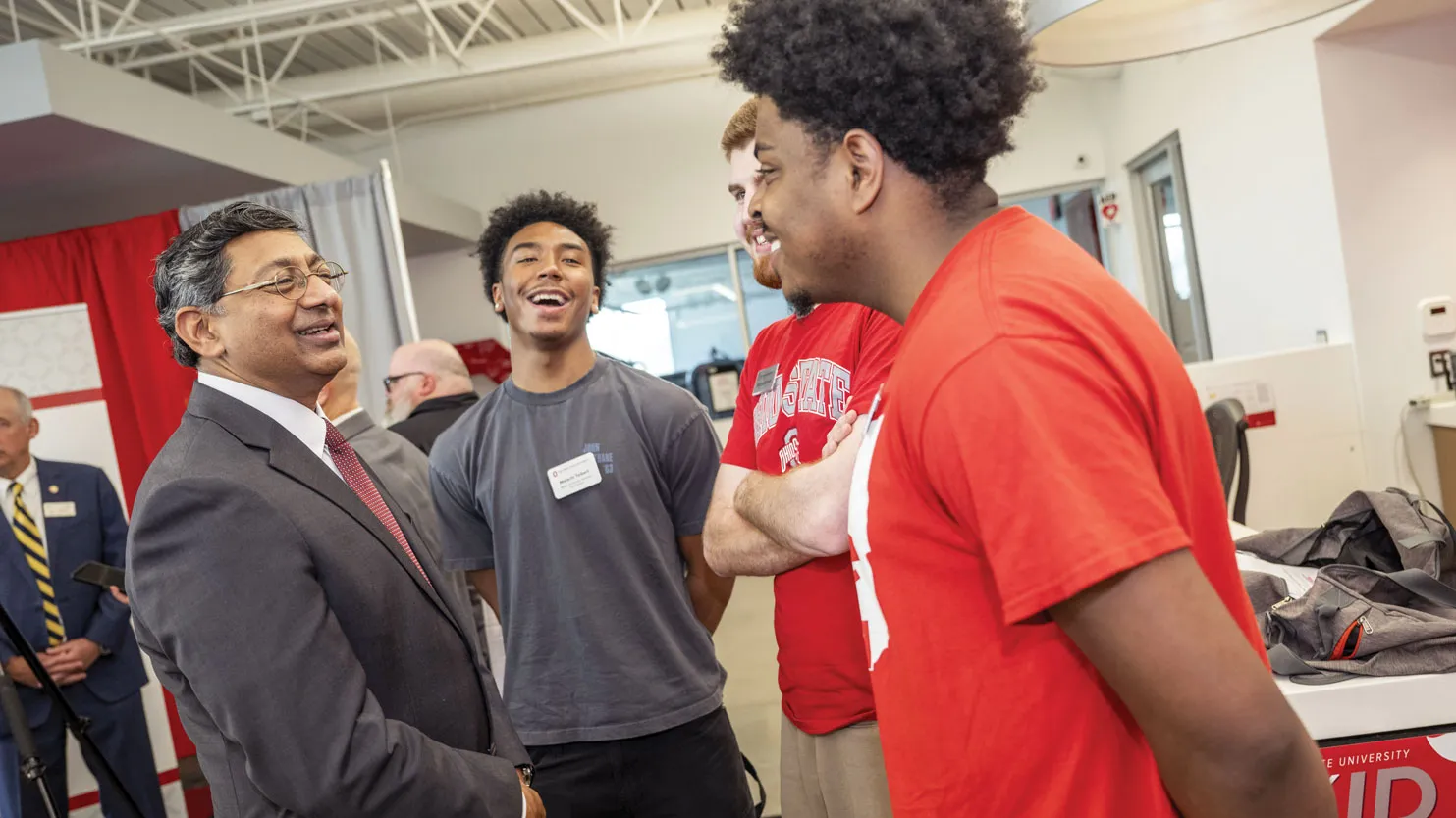 Three young men, all students, laugh as Bellamkonda chats with them in a university building.