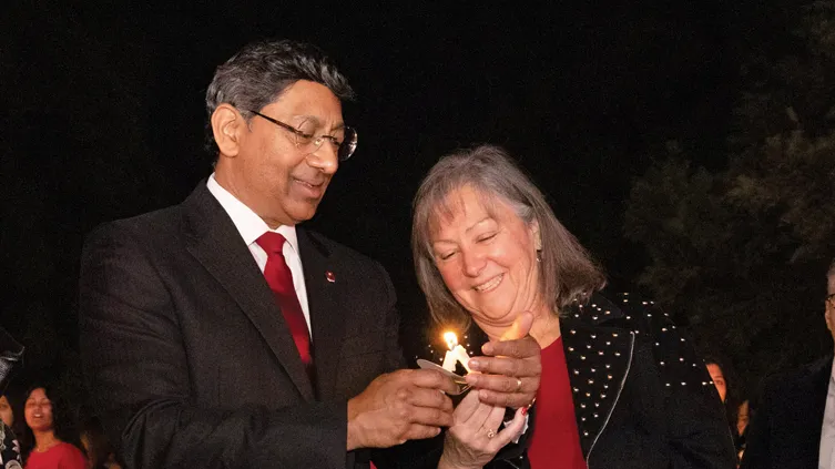 Molly Ranz Calhoun, head of the alumni association, laughs as she leans toward Ohio State President Ravi Bellamkonda to light her candle from one he holds. These are slim, about five inches long and have cardboard circles to keep wax from dripping on their hands. Bellamkonda cups his hand around the flame as he smiles and focuses.