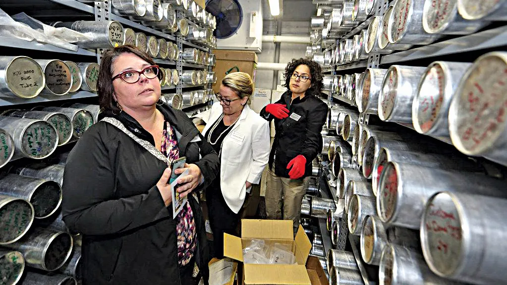 Three women stand between shelves filled with ice cores wrapped in metal. 