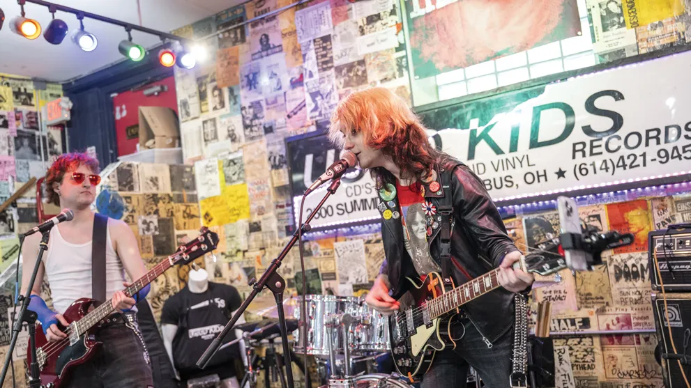 Teen band members with colorful hair play on the stage at the back of Used Kids