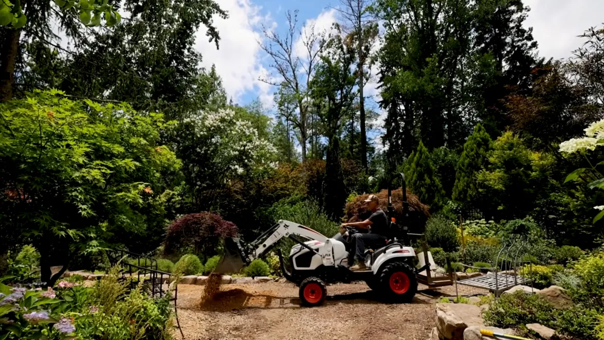 Hutchison drives a tractor down a garden path in a screenshot from the video