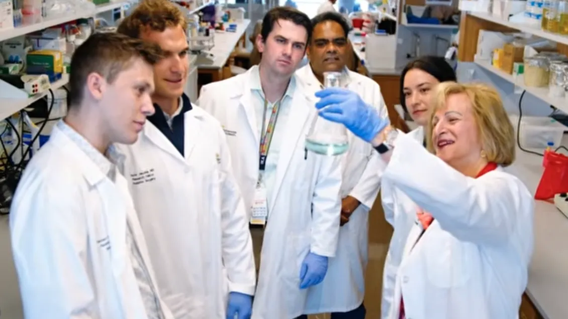 Dr. Gail Besner holds up a beaker, showing it to a group of her students