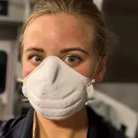 White woman with hair pulled back wearing a white facemask
