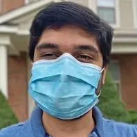 Man with short dark hair wearing a blue surgical mask