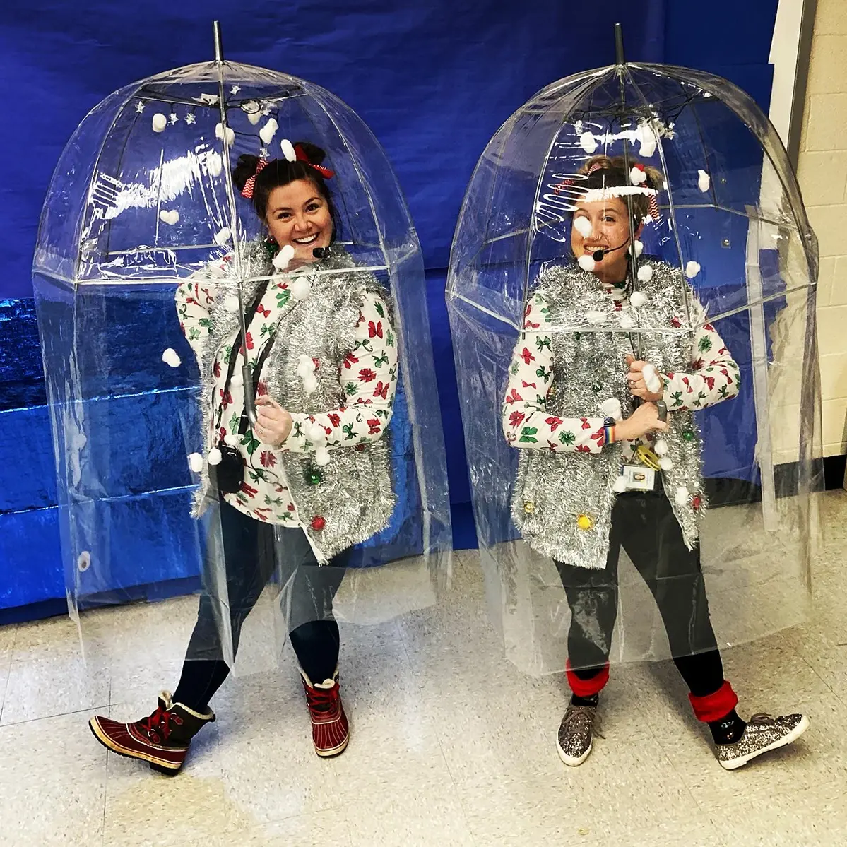 Two women wear shiny costumes and stand within clear plastic bubbles made from umbrellas