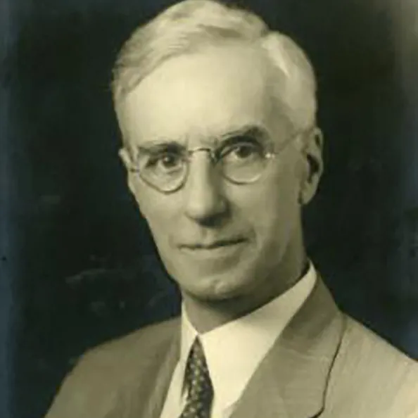 George Rightmire had a tall face, thin-framed glasses and white hair. He wears a suit and tie.