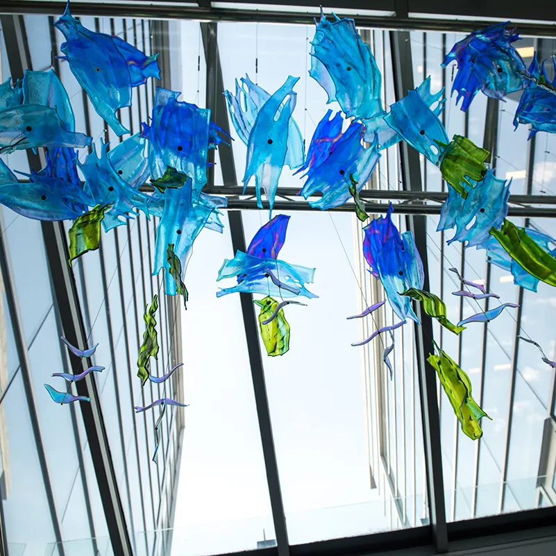 transparent, water-colored glass shapes hang from a glass roof inside a building