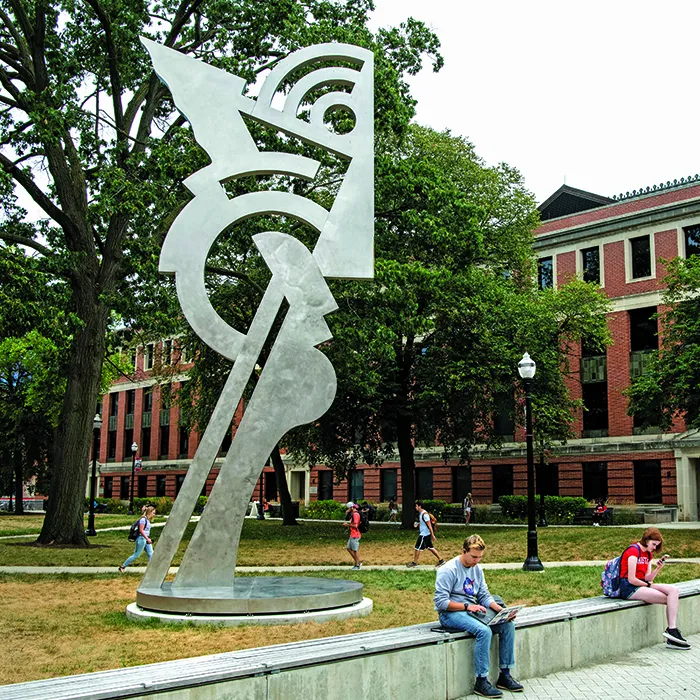 A largemetal sculpture shows a stylized face and is four or five people tall
