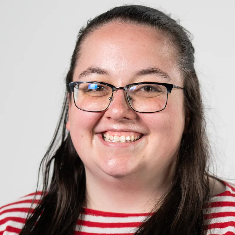 Becca Young smiles in glasses and a scarlet and white striped shirt