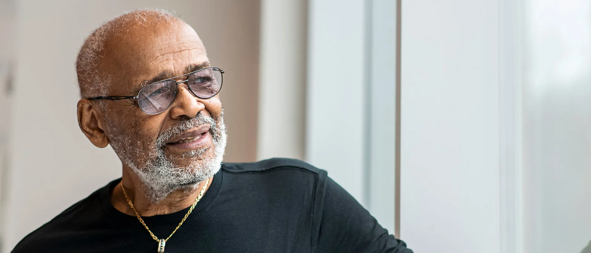 An older black man with gray hair and glasses seems thoughtful as he looks into the distance