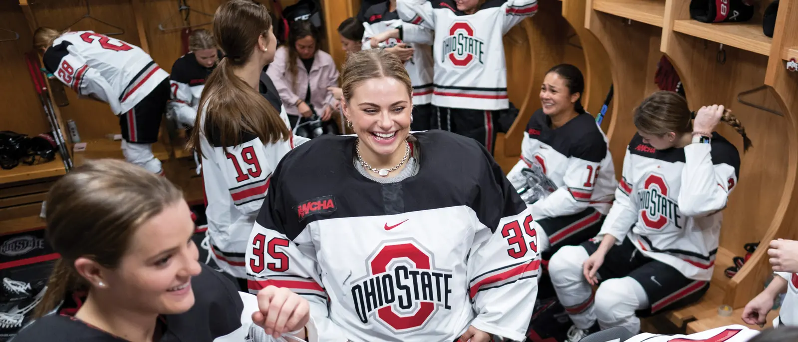 In a crowded locker room, young women in ponytails and Ohio State hockey uniforms laugh and talk in groups.
