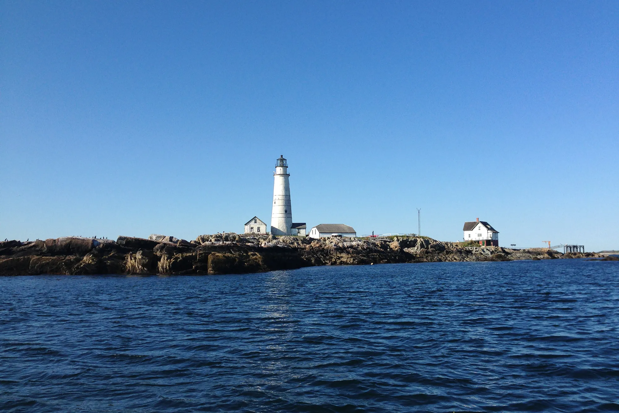 A lone lighthouse rises on a spit of land along water.