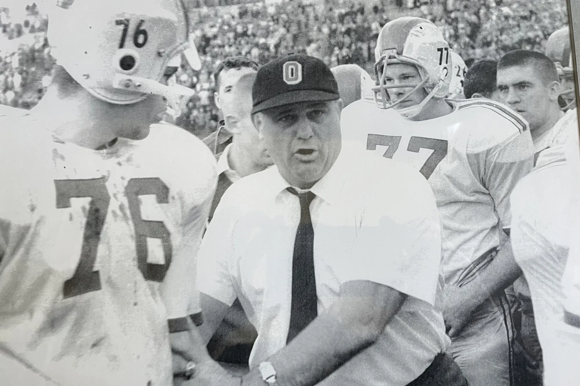 On the sidelines of a football game, famous Ohio State coach Woody Hayes holds the arm of a football player he’s talking to. The player watches him, but he looks straight ahead. Behind them, the player featured in this story intently watches something on the field.