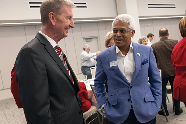 President Carter shats with a man of Indian descent inside a conference room and amid a crowd. They're both smiling as they talk.